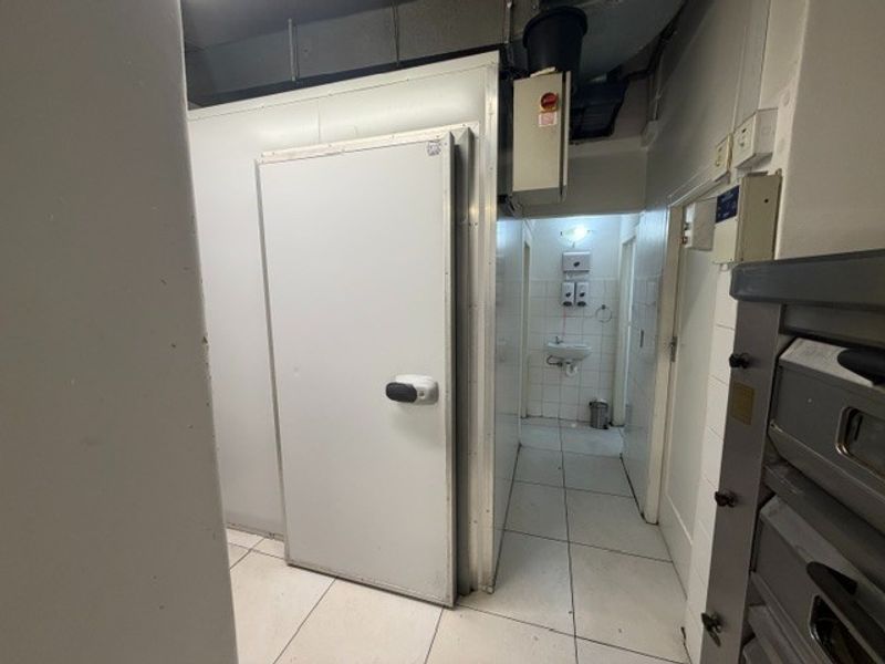 Utility area featuring a walk-in cold storage unit, tiled flooring, and a small hand-wash basin, suitable for commercial kitchen operations.