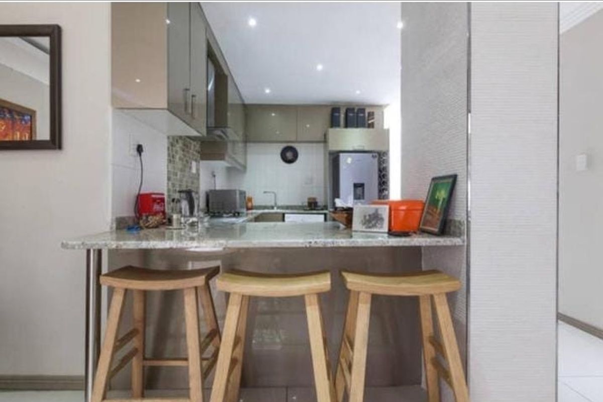 A compact, modern kitchen featuring a granite breakfast bar, sleek cabinetry, and a mosaic tile backsplash, providing a functional and stylish cooking space.