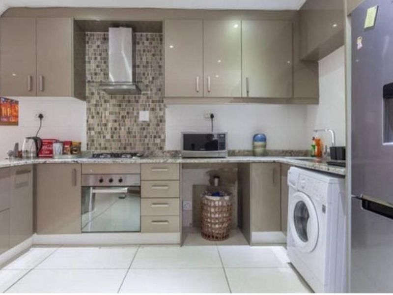 Modern kitchen featuring high-gloss cabinetry, granite countertops, mosaic tile backsplash, integrated oven, gas hob, and dedicated space for laundry appliances.