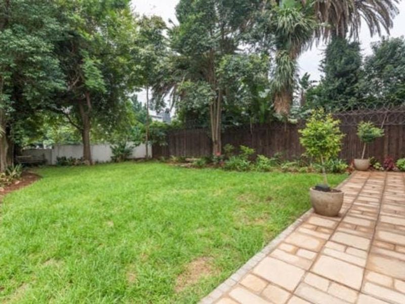 A private garden area featuring a paved patio, established trees, and a secure timber fence boundary.