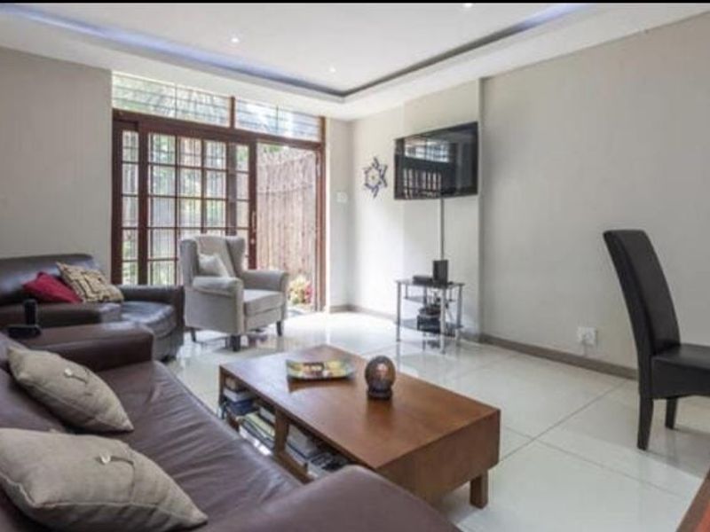 A bright living room featuring tiled flooring, recessed ceiling lighting, and a sliding glass door providing access to an outdoor area.
