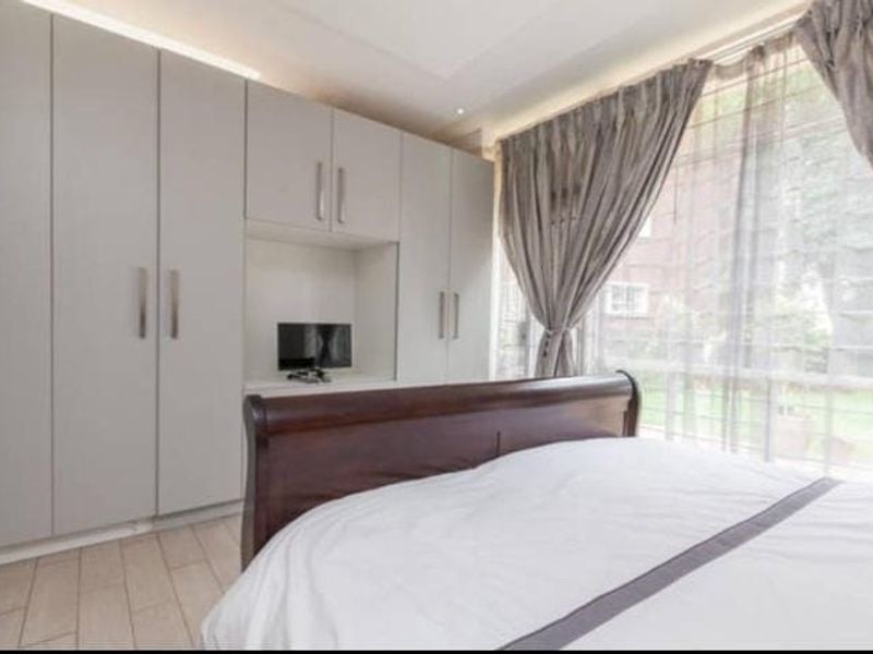 A well-lit bedroom featuring extensive floor-to-ceiling built-in cupboards with a central recessed niche and modern tiled flooring.