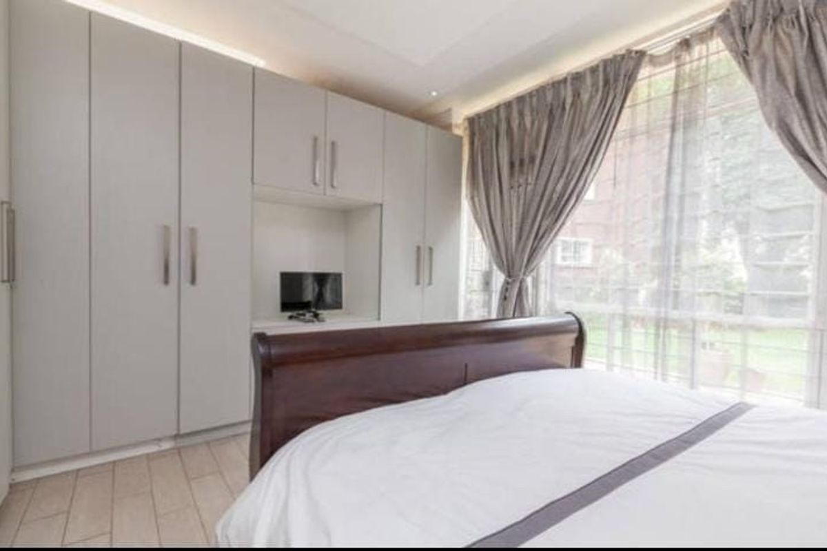 A well-lit bedroom featuring extensive floor-to-ceiling built-in cupboards with a central recessed niche and modern tiled flooring.