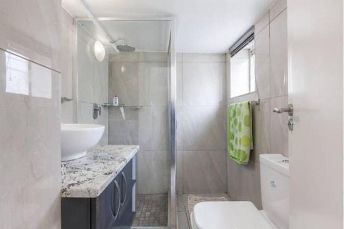 A compact bathroom featuring a modern vanity with granite countertop, vessel sink, and a glass-enclosed shower with tiled finishes.