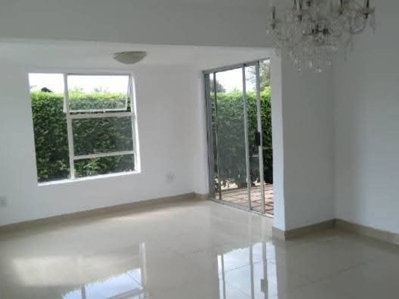 A bright, empty living area featuring polished tiled flooring, large windows, and a sliding glass door providing access to the outdoor space.