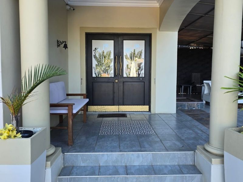 A welcoming covered entrance featuring a double front door, tiled steps, and decorative columns under a classic archway.