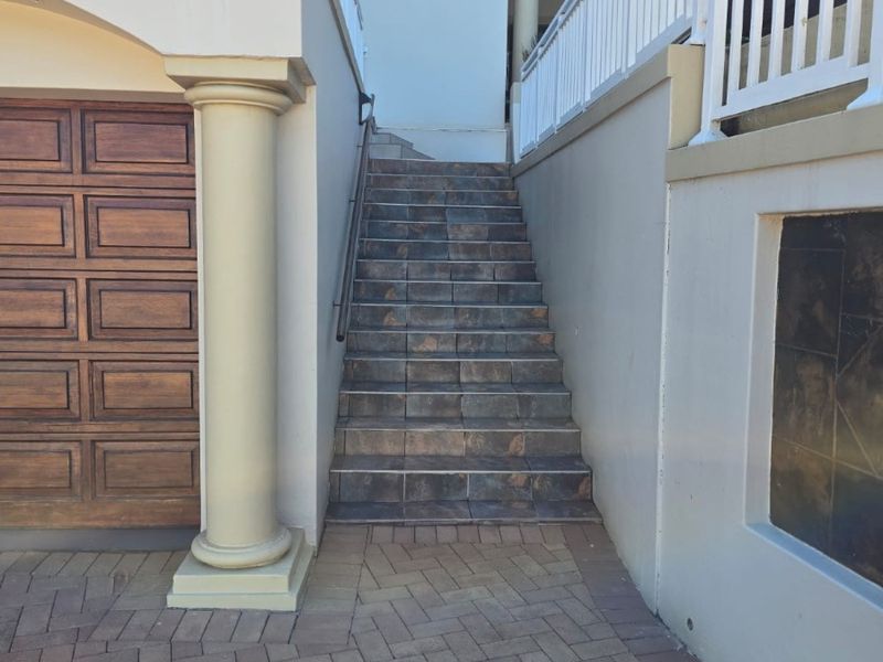 Front entrance area featuring a paved driveway, a tiled staircase with a metal handrail, and a wooden garage door.
