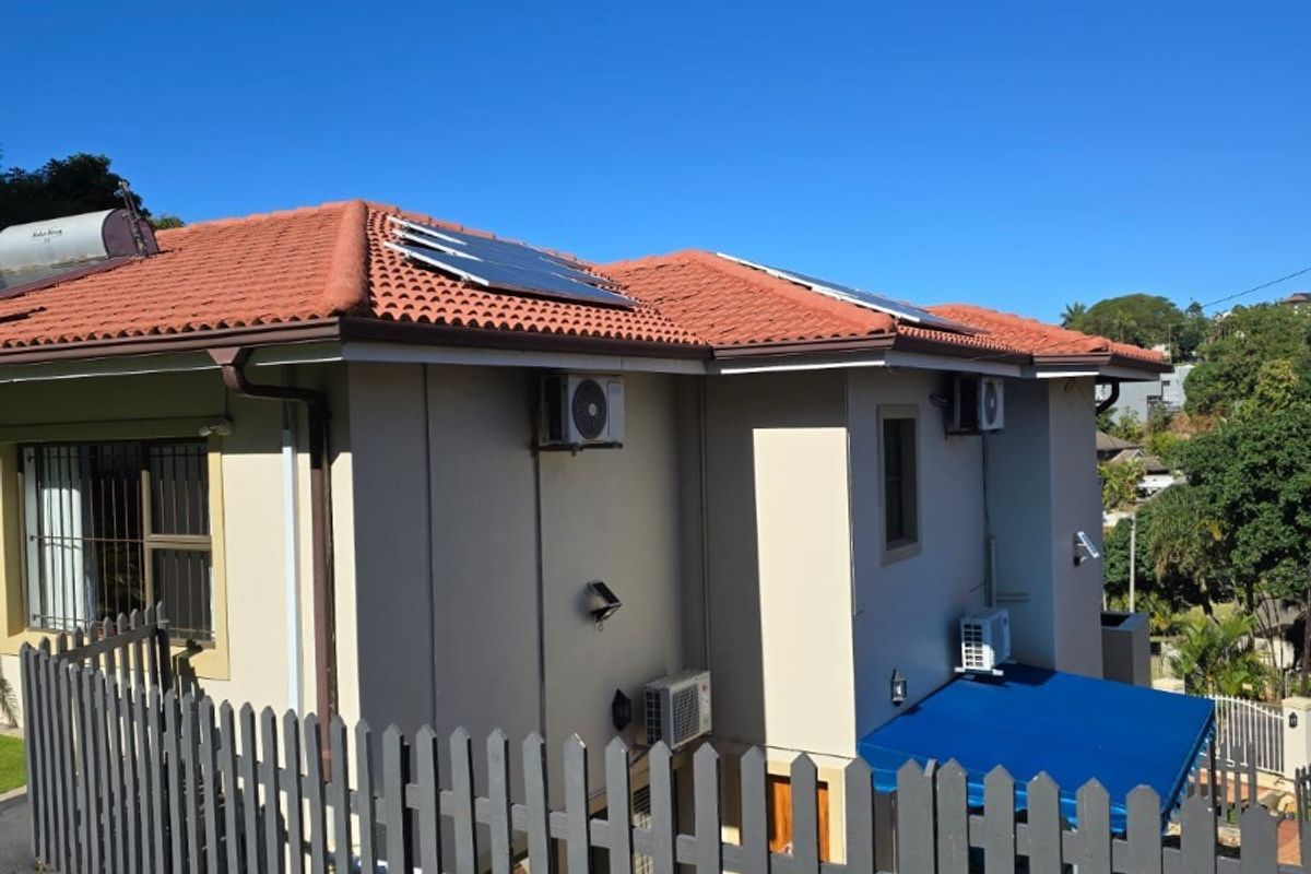 Rear view of the property featuring terracotta roof tiles, installed solar panels, solar geyser, multiple air conditioning units, and a secure picket fence.