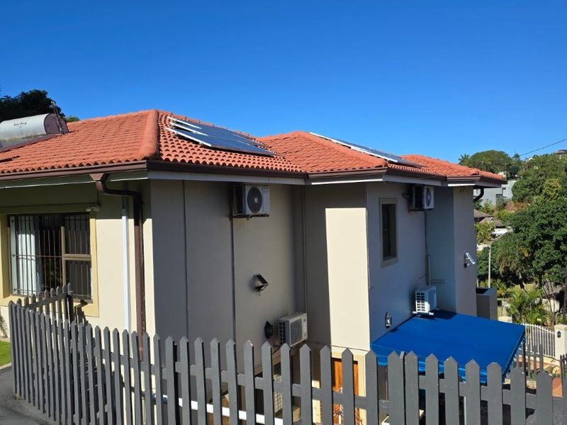 Rear view of the property featuring terracotta roof tiles, installed solar panels, solar geyser, multiple air conditioning units, and a secure picket fence.