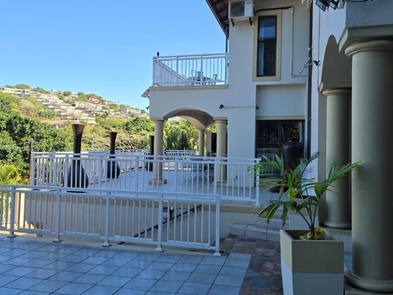 Spacious multi-level outdoor patio and balcony area featuring tiled flooring, structural columns, and white balustrades with views of the surrounding landscape.