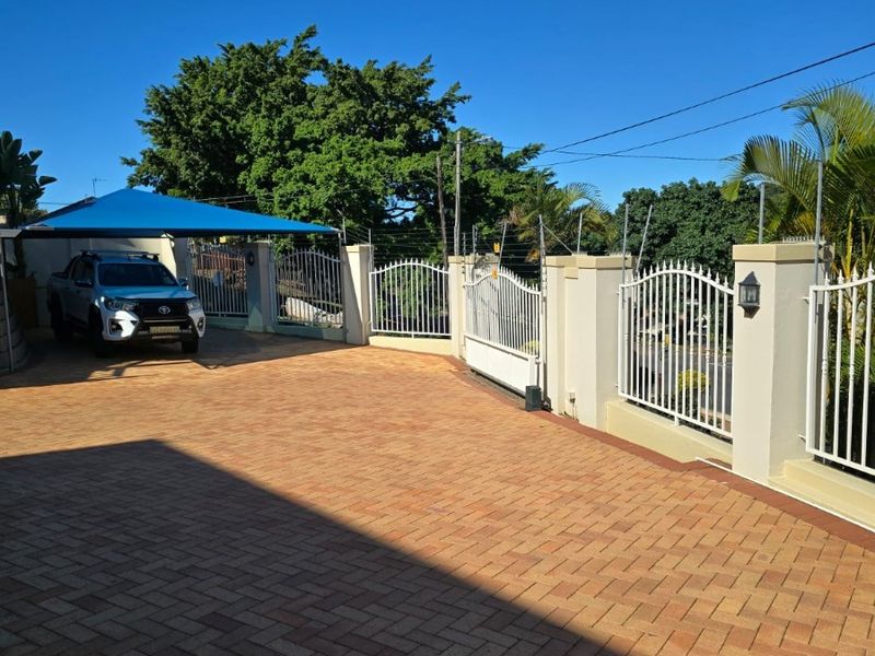 A well-maintained front driveway featuring paved surfaces, secure perimeter walling with metal fencing, an electric fence, and a functional shade cloth carport.
