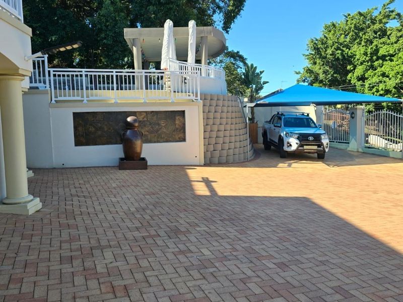 Spacious paved driveway leading to a raised patio area with a shade sail and decorative retaining wall features.