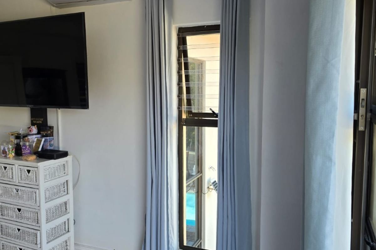 A bright living area featuring polished marble-look floor tiles, a wall-mounted air conditioning unit, and a tall casement window with modern curtains.