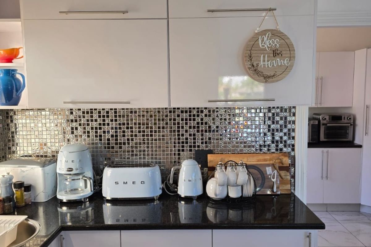 Modern kitchen featuring glossy white cabinetry, a contrasting black granite countertop, and a decorative mosaic tile backsplash.