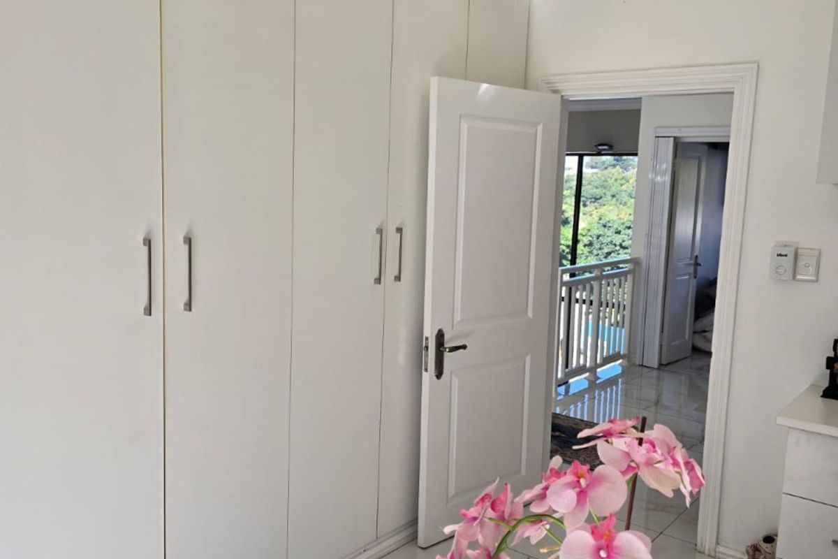 A bright bedroom featuring extensive built-in cupboards, tiled flooring, and a ceiling fan, with a doorway leading to an adjacent hallway.