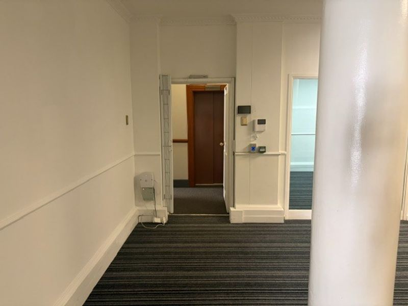 A clean, empty office hallway featuring carpeted flooring, a structural column, and classic architectural details including crown molding and wainscoting.