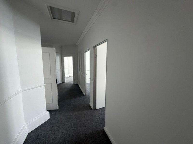 A clean, neutral hallway featuring wainscoting, ceiling cornicing, and dark carpet flooring, providing access to multiple office rooms.