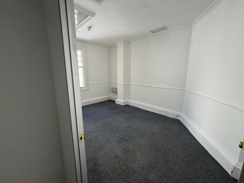 A clean, empty office space featuring neutral walls, carpeted flooring, and classic crown molding details.