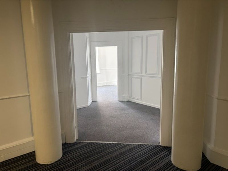An empty office space featuring decorative columns, wainscoting, and neutral carpeting, offering a clean and professional layout.