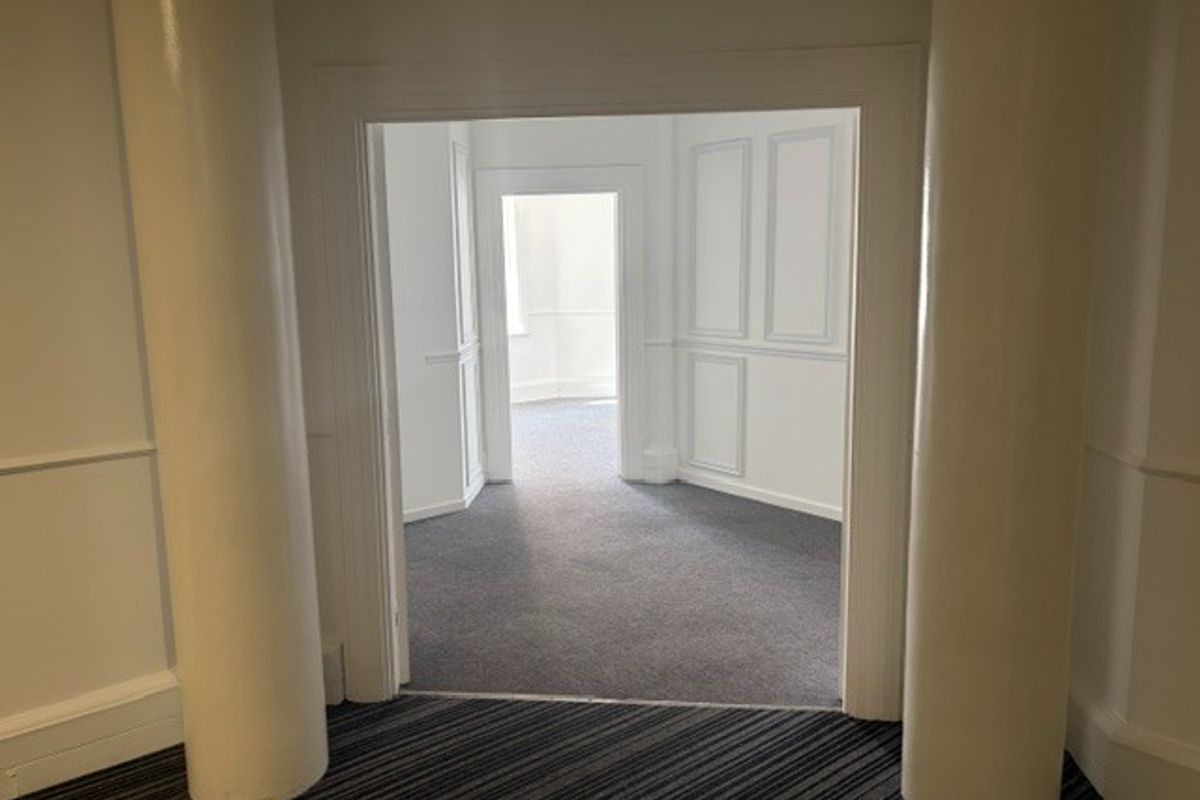 An empty office space featuring decorative columns, wainscoting, and neutral carpeting, offering a clean and professional layout.