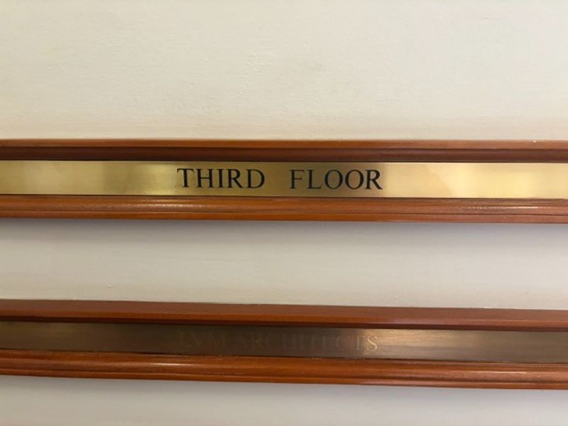 A close-up view of a brass third-floor office directory sign mounted on a wall with timber trim detailing.