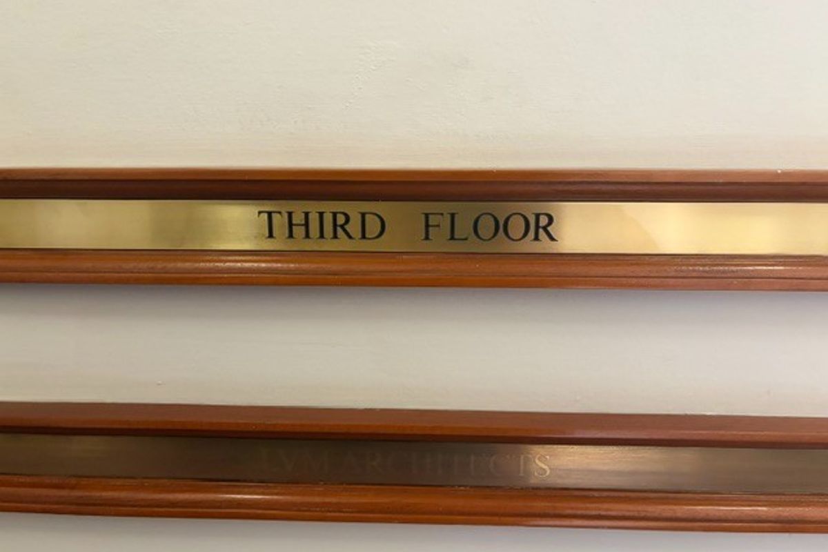 A close-up view of a brass third-floor office directory sign mounted on a wall with timber trim detailing.
