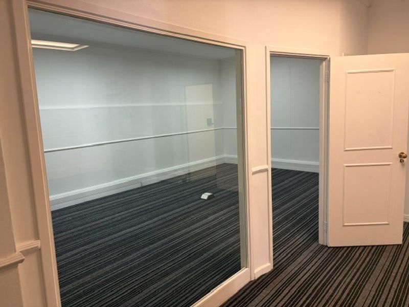 An empty office space featuring a glass partition, striped carpeting, and a classic panelled door, offering a clean and professional environment.
