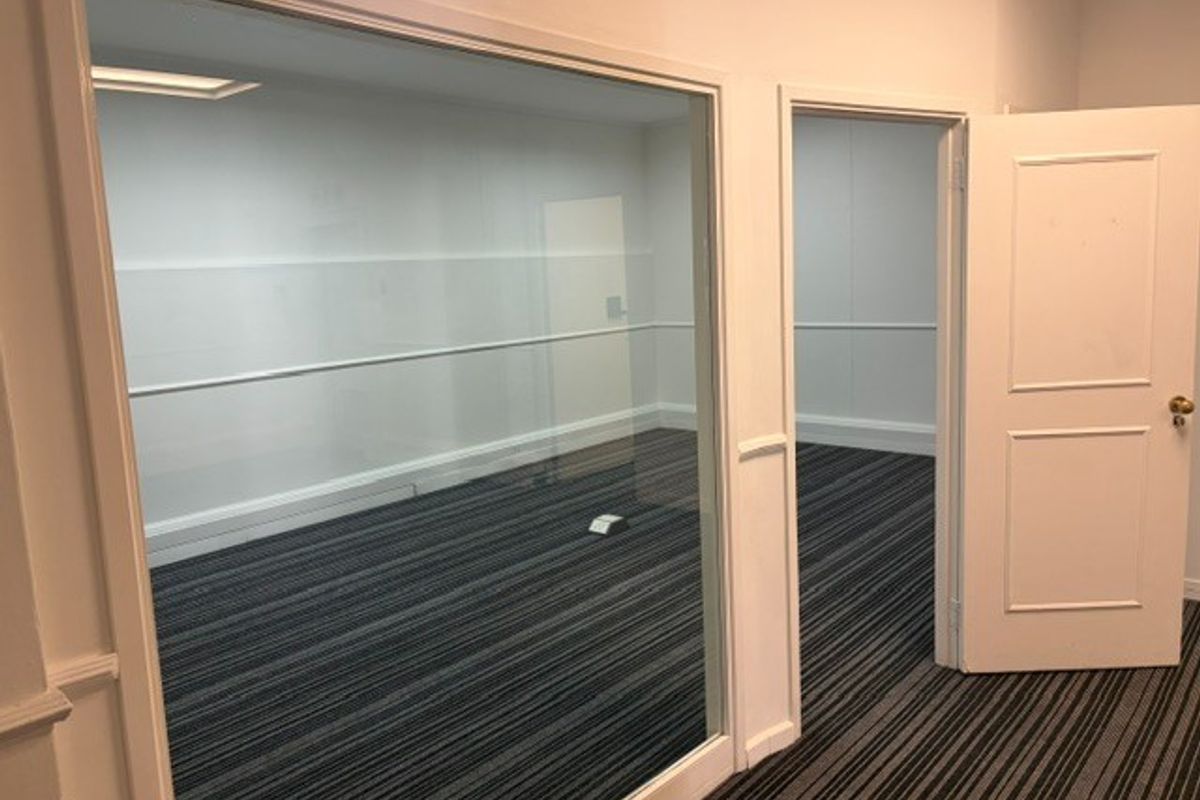 An empty office space featuring a glass partition, striped carpeting, and a classic panelled door, offering a clean and professional environment.