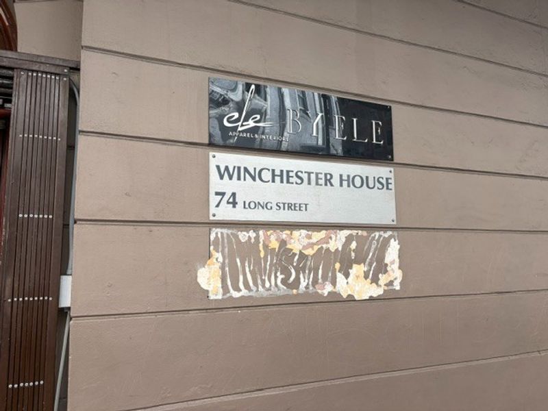 Exterior facade detail showing building signage for Winchester House at 74 Long Street, featuring visible paint damage on the wall surface.