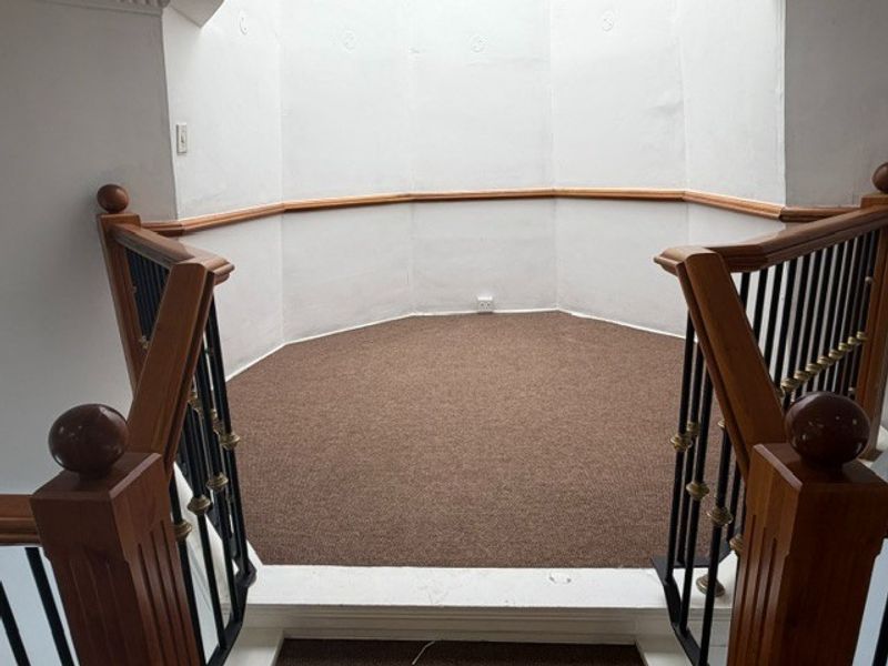 A vacant landing area featuring a wooden handrail with metal balustrades and carpeted flooring, providing access to the upper level of the office.