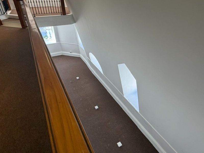 A spacious, carpeted hallway featuring a wooden handrail, metal balustrade, and unique recessed windows along the sloped wall.