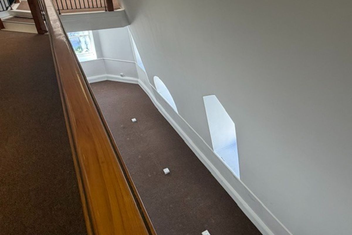 A spacious, carpeted hallway featuring a wooden handrail, metal balustrade, and unique recessed windows along the sloped wall.