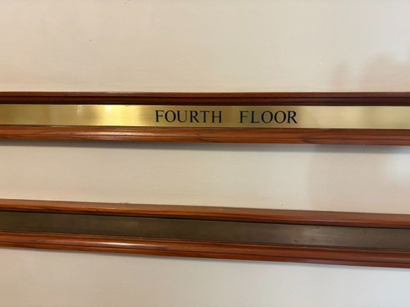 A close-up view of a fourth-floor brass signage plaque mounted on a wall with decorative timber trim.