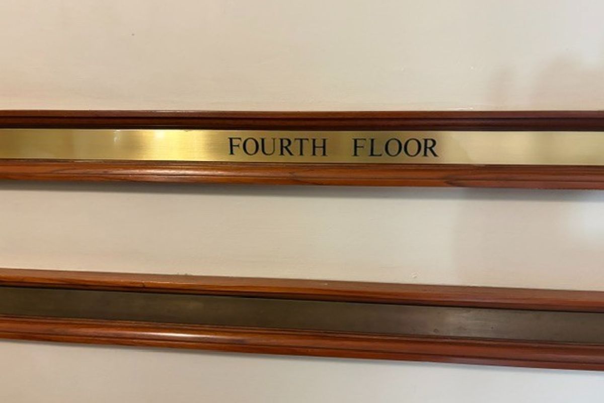 A close-up view of a fourth-floor brass signage plaque mounted on a wall with decorative timber trim.
