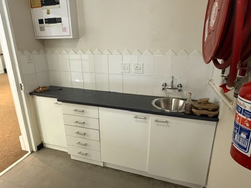 A functional utility area featuring built-in cabinetry, a stainless steel sink, tiled backsplash, and essential fire safety equipment including a hose reel and extinguisher.
