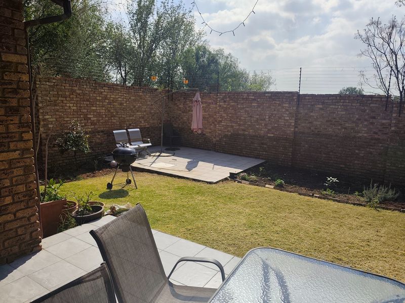 A private rear garden featuring a paved patio area, established lawn, and secure brick boundary walls with electric fencing.