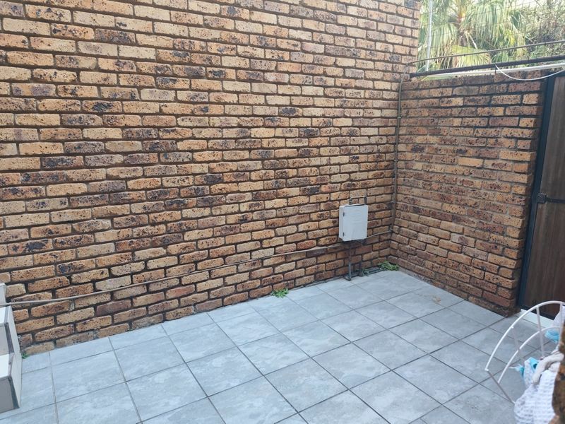A private rear courtyard area featuring face brick walls and tiled flooring, suitable for a small outdoor seating space.