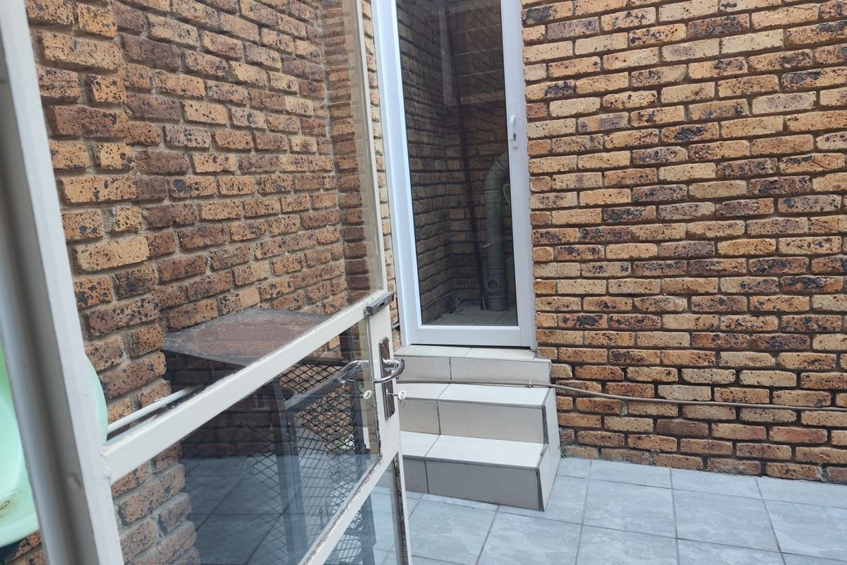 A small, enclosed rear courtyard area featuring face brick walls, tiled flooring, and a set of steps leading to a glass-paneled door.