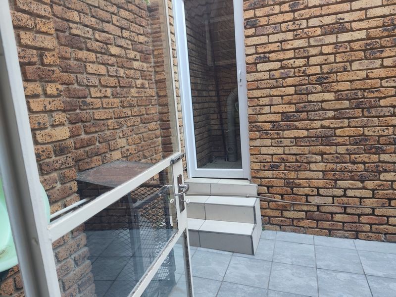 A small, enclosed rear courtyard area featuring face brick walls, tiled flooring, and a set of steps leading to a glass-paneled door.