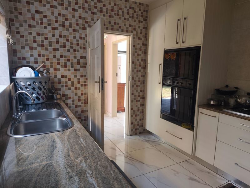 A functional kitchen featuring granite countertops, a double bowl sink, built-in double oven, and mosaic tile backsplash with modern floor tiles.