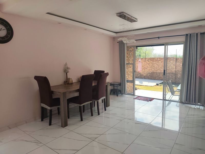Bright dining area featuring polished marble-look floor tiles, a modern crystal chandelier, and large sliding glass doors providing direct access to the rear patio.