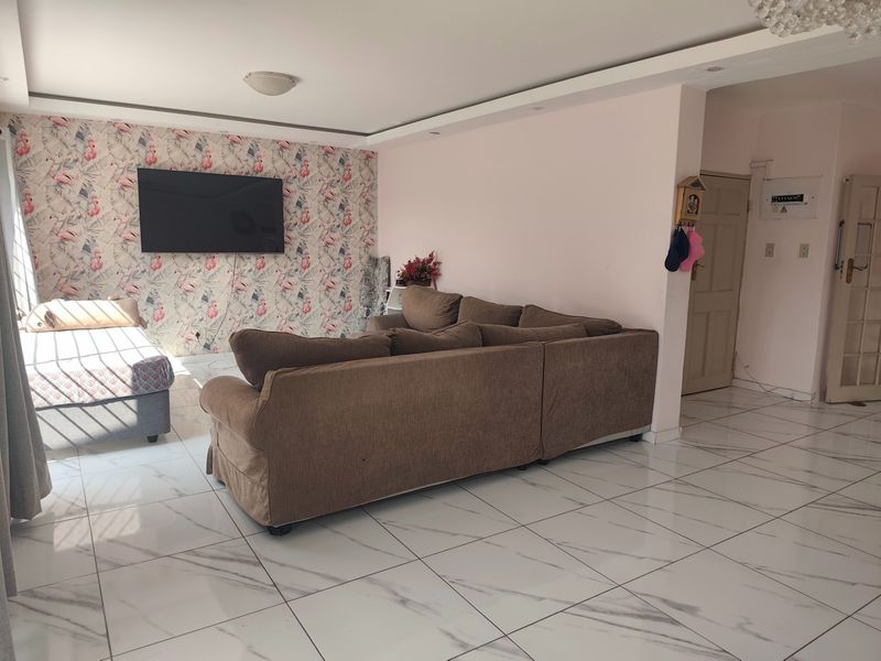 Spacious living area featuring modern white marble-look porcelain floor tiles, a decorative feature wall, and recessed ceiling lighting.