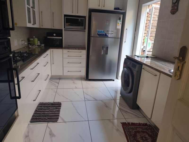 Modern kitchen featuring white cabinetry, granite countertops, gas hob, built-in oven, and sleek tiled flooring with a clean, functional layout.