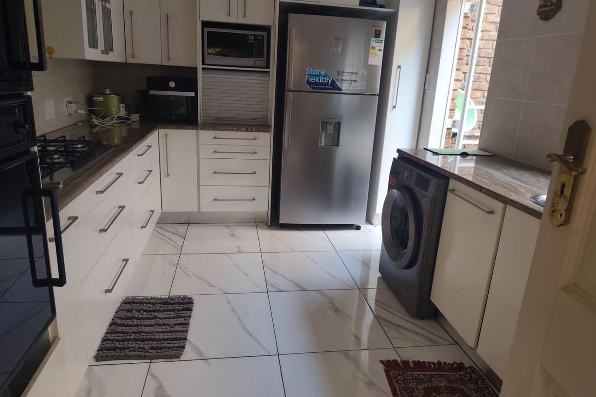 Modern kitchen featuring white cabinetry, granite countertops, gas hob, built-in oven, and sleek tiled flooring with a clean, functional layout.