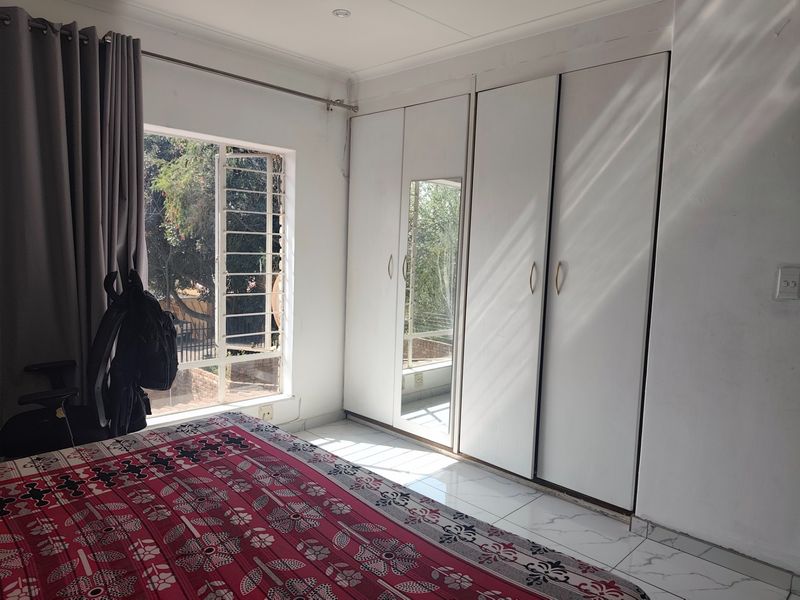 A bedroom featuring built-in cupboards with a mirrored panel, tiled flooring, and a window with security bars.