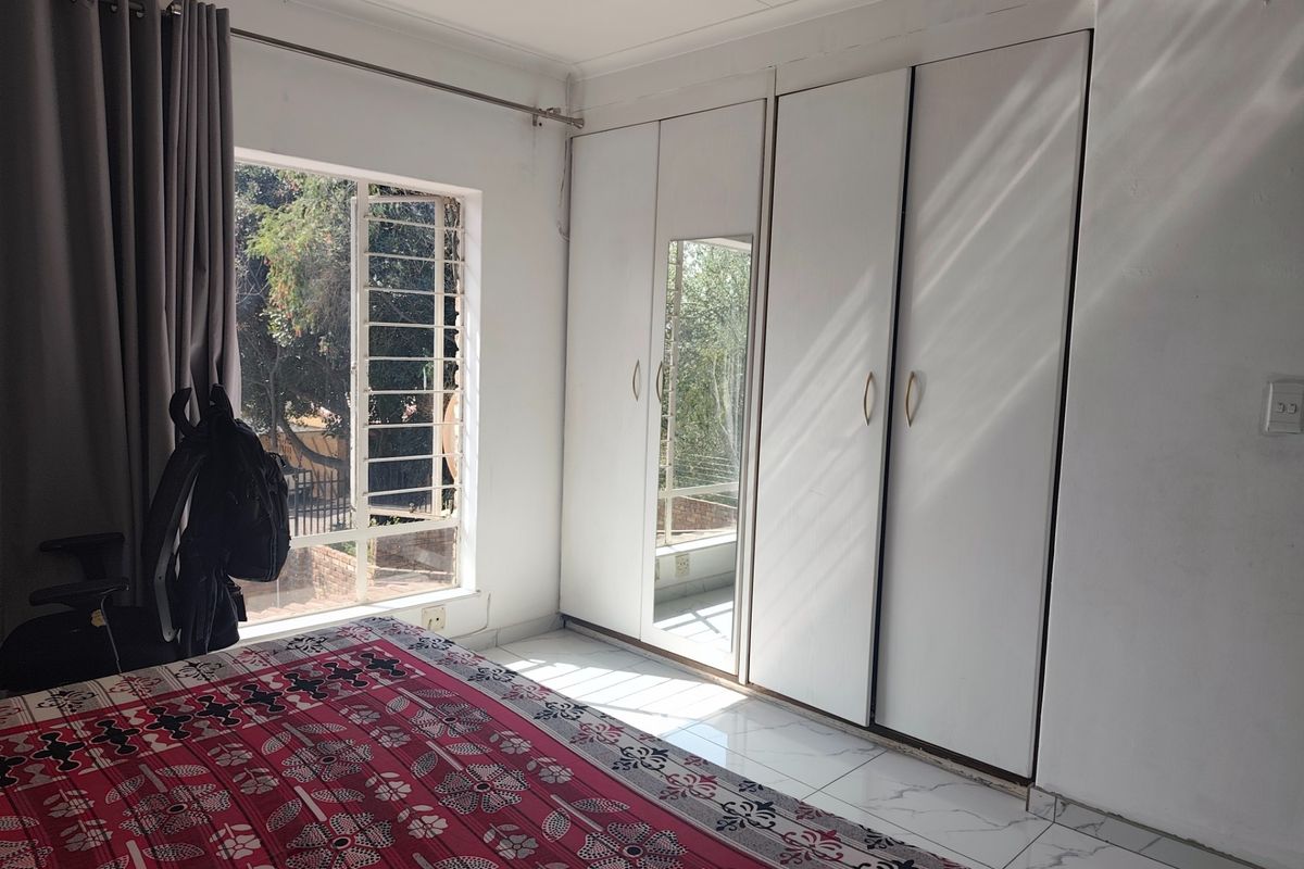 A bedroom featuring built-in cupboards with a mirrored panel, tiled flooring, and a window with security bars.