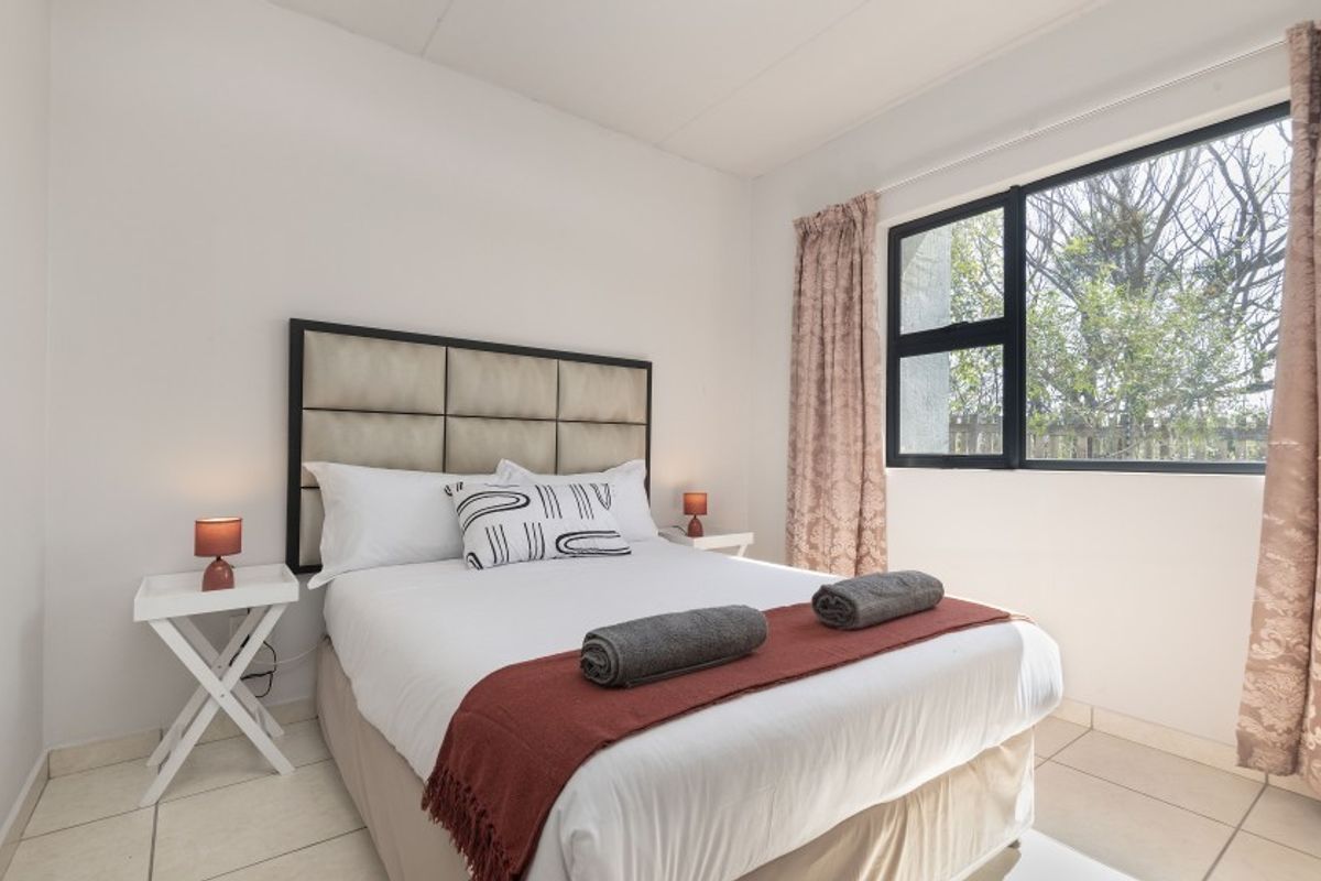 A well-lit bedroom featuring neutral tiled flooring and a large aluminium-framed window providing natural light and garden views.