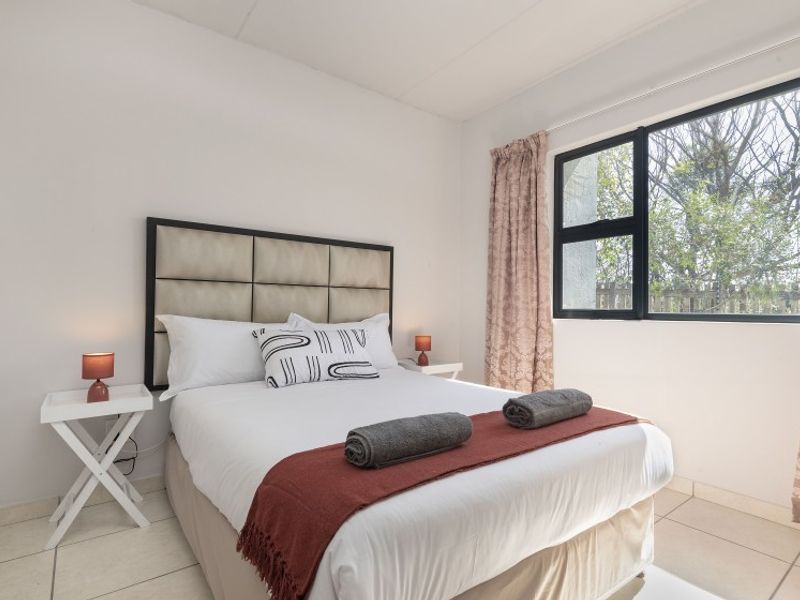 A well-lit bedroom featuring neutral tiled flooring and a large aluminium-framed window providing natural light and garden views.