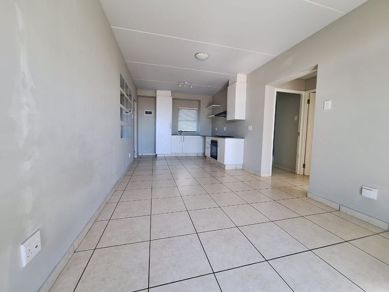 An open-plan living and kitchen area featuring tiled flooring, built-in cabinetry, and integrated appliances, currently vacant and awaiting finishing touches.