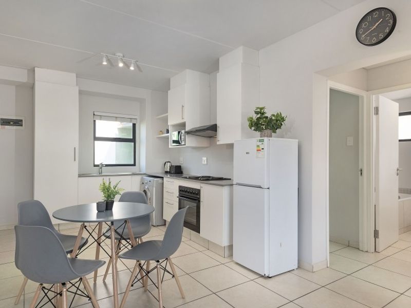 Open-plan kitchen and dining area featuring white cabinetry, built-in oven and hob, tiled flooring, and direct access to the bathroom.